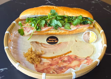 Banh mi sandwich with fresh cilantro on baguette served on tray with sliced meats and pâté.