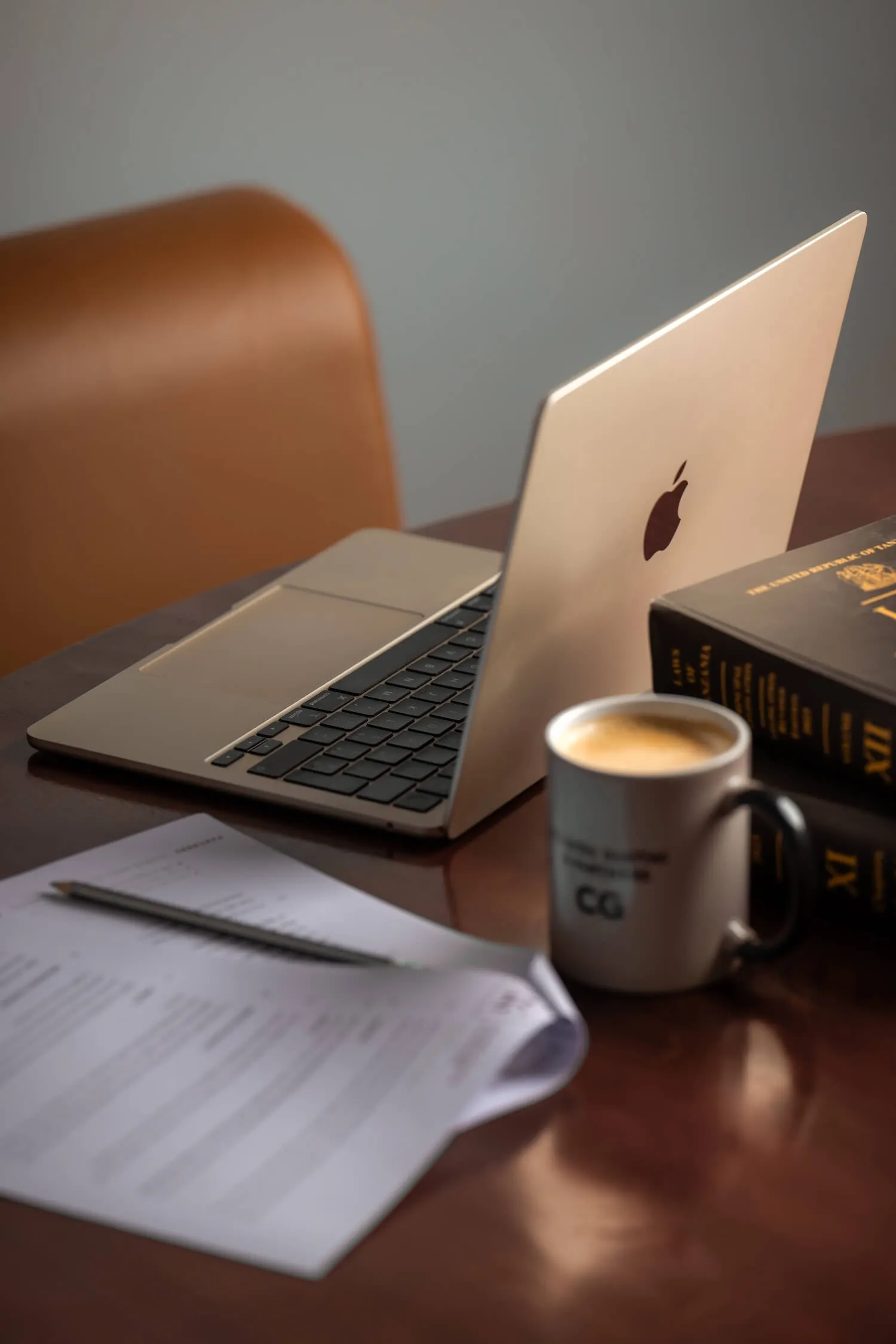 Laptop on table with paperwork, pencil, coffee mug, and two thick books stacked.
