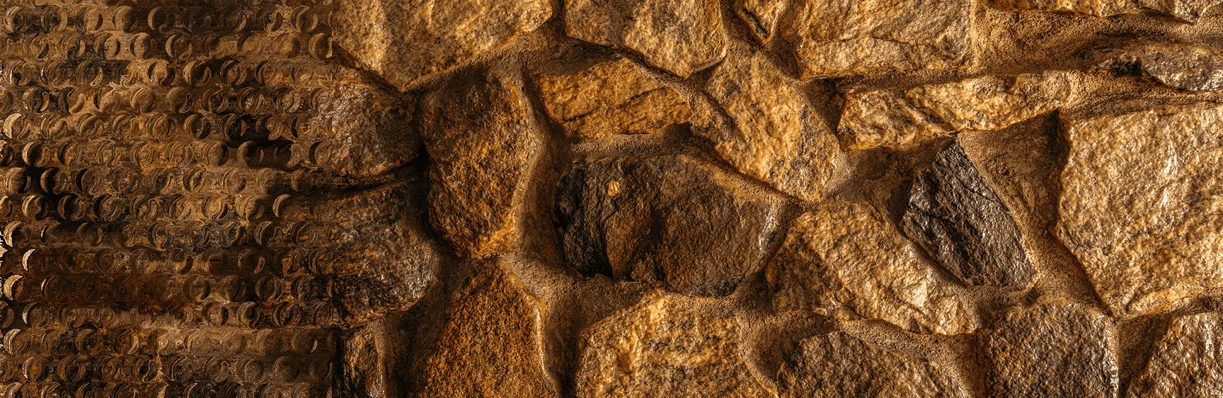 Close-up of textured brown and tan stone wall with rough, uneven surfaces and mortar.