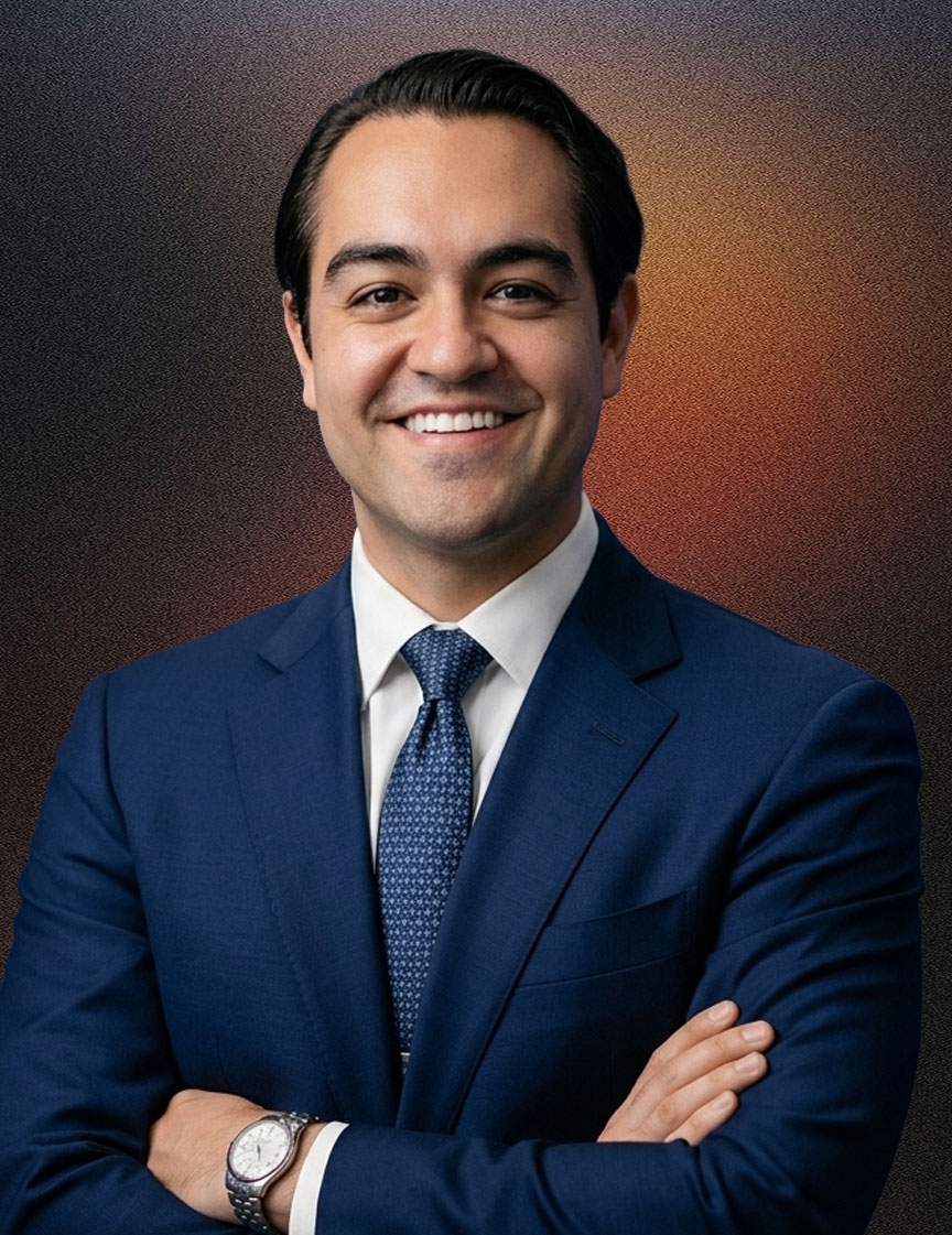 Man with glasses in a green suit jacket, white shirt, and green tie, smiling with arms crossed against a plain dark background.