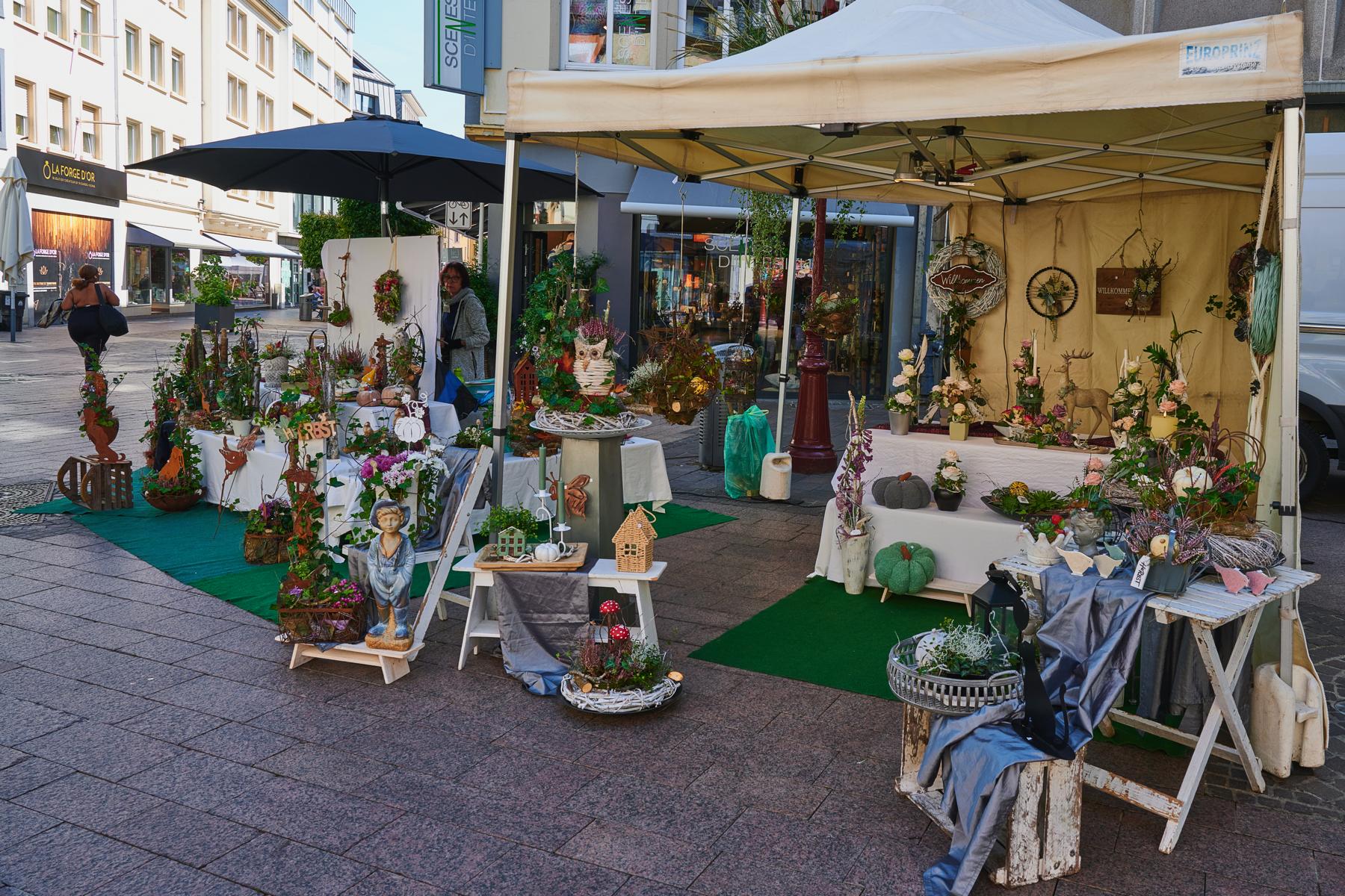 Outdoor market stall with floral arrangements, decorative plants, and handcrafted rustic ornaments.