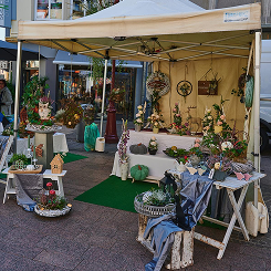 Outdoor market stall with floral arrangements and decorative plants under a yellow canopy.