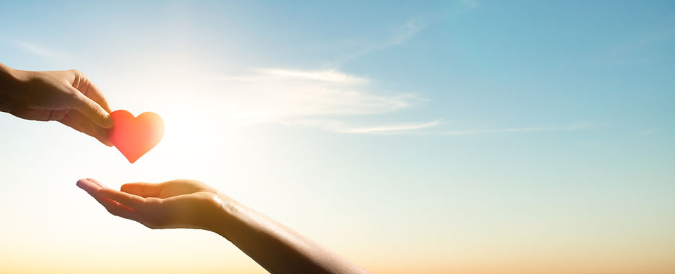 Hands exchange a red heart shape against a bright sky with a sunrise glow, symbolizing love and kindness, which is what we are all about at The Center for Adult Dentistry