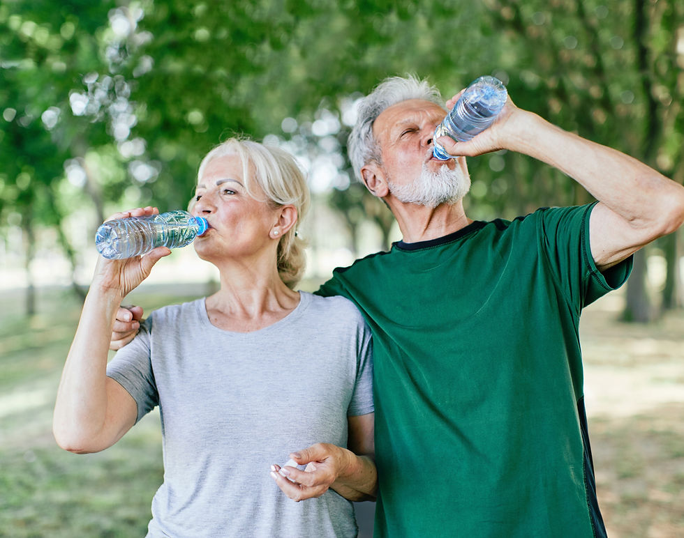 Older couple in a park drinks from water bottles because of the importance of hydration for oral health