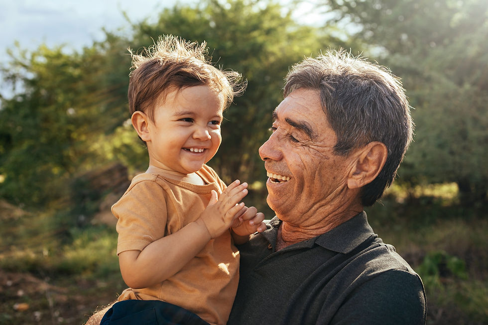 Elderly man holding a young child outdoors, both smiling happily.
