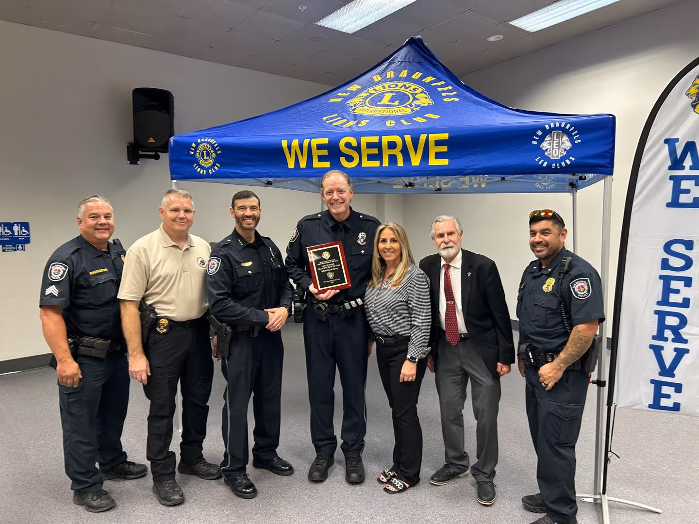 Group of police officers and two civilians standing under a blue Lions Club tent holding a plaque.