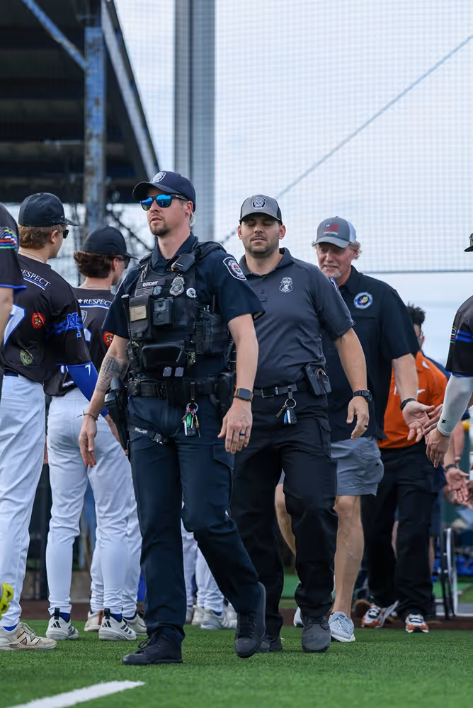Police officers walking on a baseball field near players shaking hands after a game.