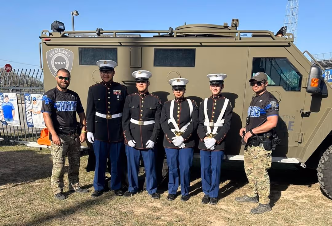 Group of four Marines in dress uniforms and two officers in tactical gear stand in front of a SWAT vehicle.