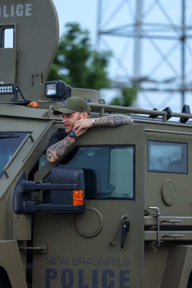 Man with tattoos and cap leaning out of New Braunfels Police armored vehicle door.