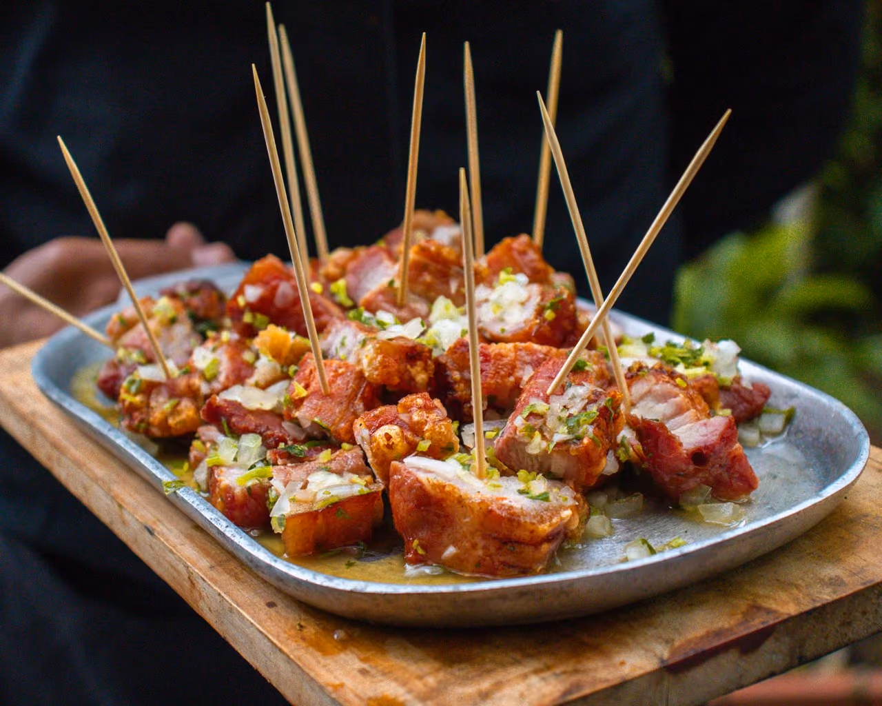 Plate of crispy pork bites with chopped onions and herbs served with wooden toothpicks.