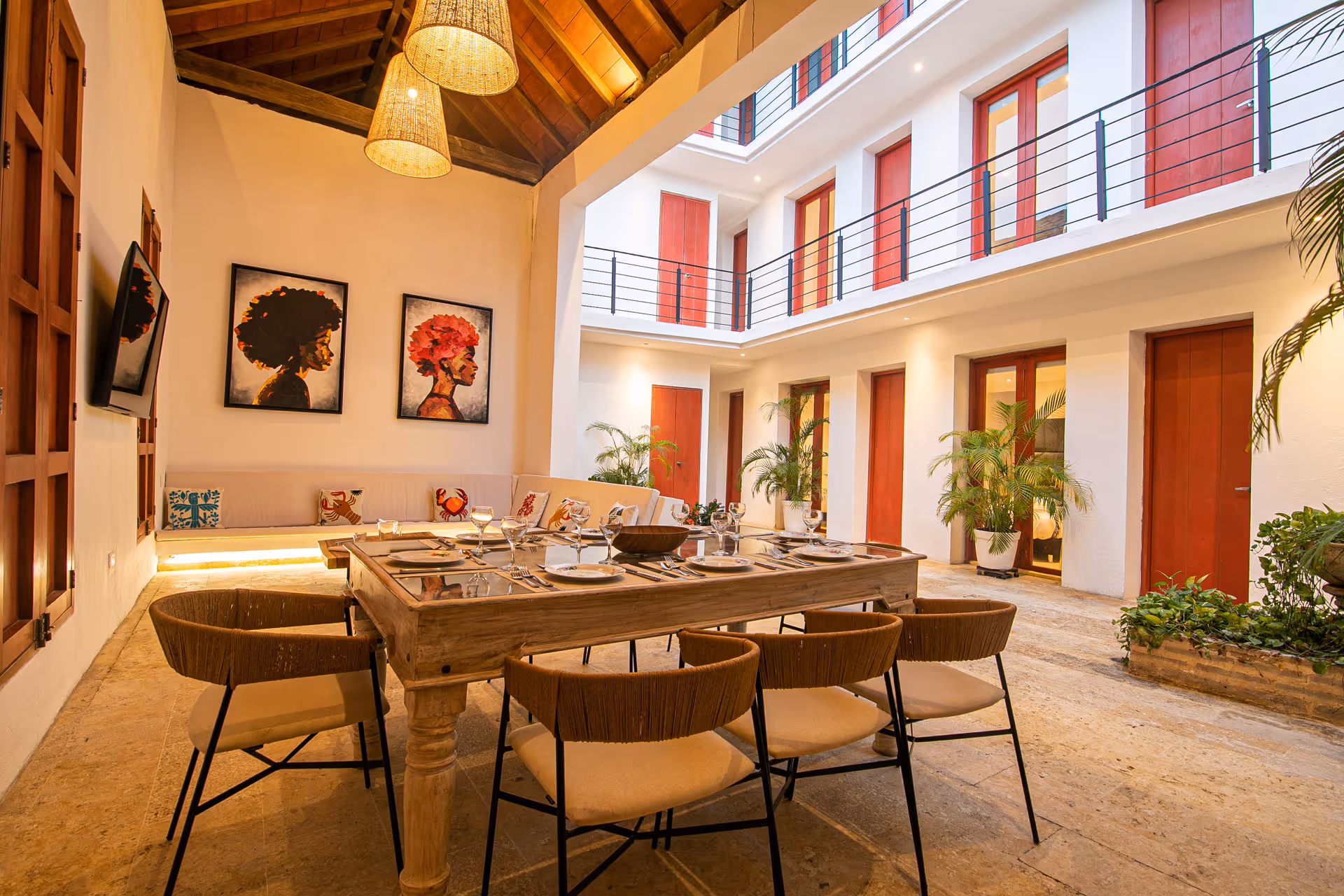 Open-air dining area with a wooden table set for eight, surrounded by chairs and vibrant art on walls.