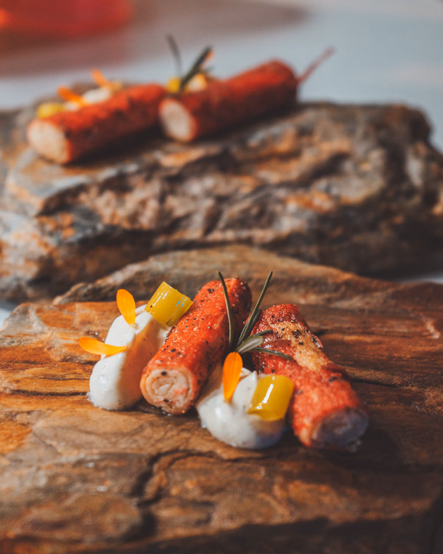 Gourmet dish with rolled meat, creamy sauce, yellow garnish, and herbs on a rustic stone plate.