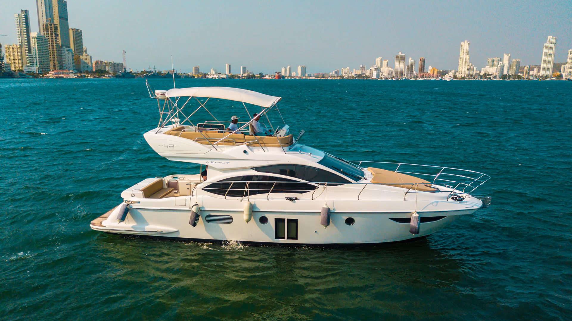 White Azimut 42 yacht cruising on blue water with city skyline in the background.