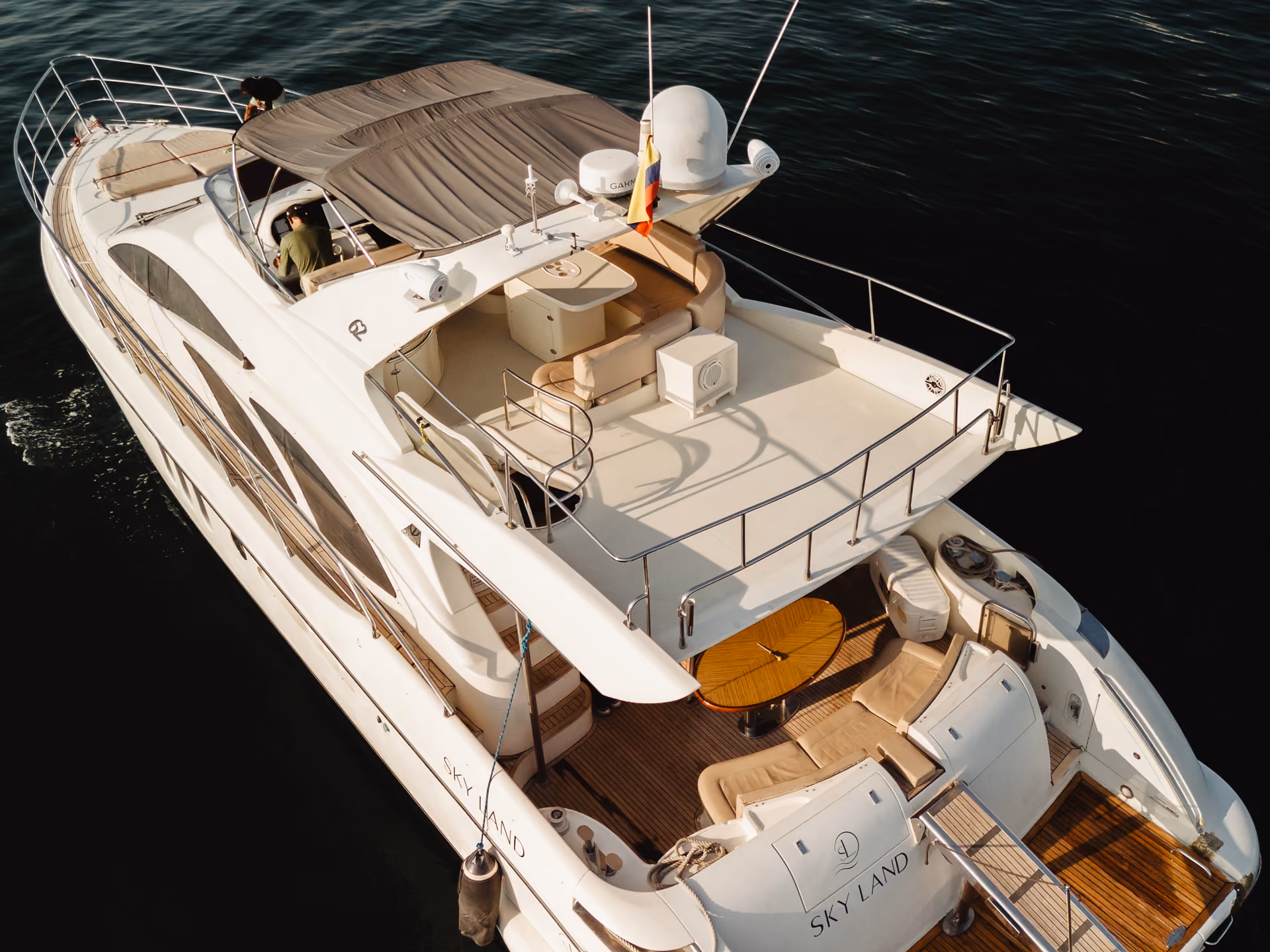 White luxury yacht named Sky Land with sunshade, seating areas, and a wooden deck on calm dark water.