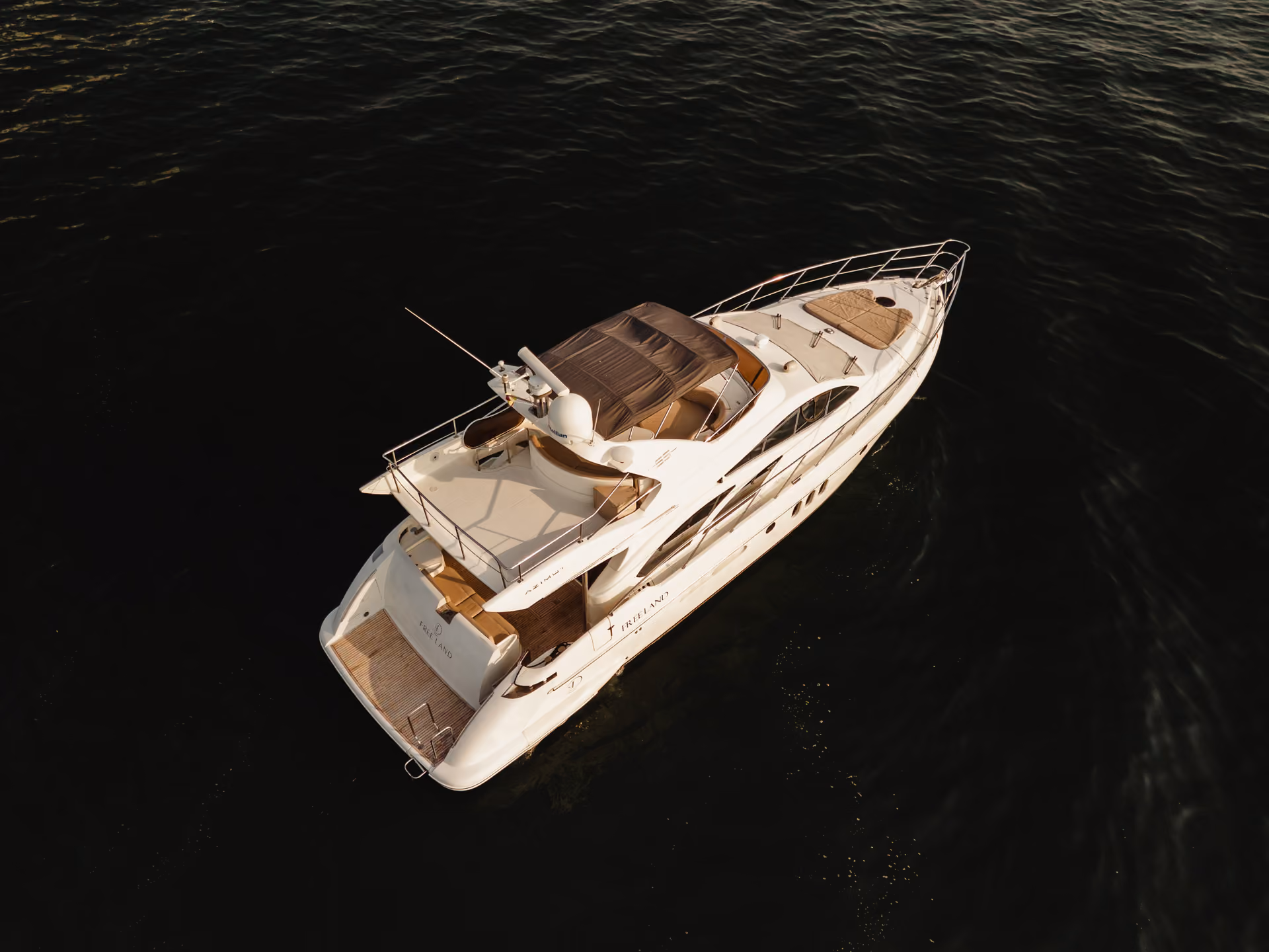 A white luxury yacht with a sun deck and shaded seating floats on dark water.