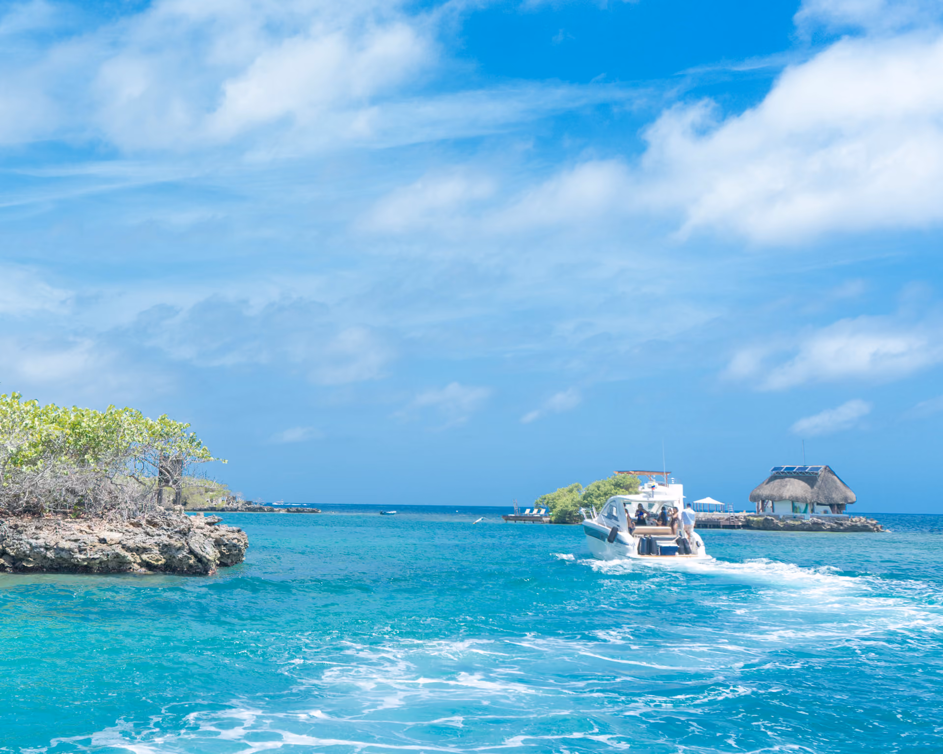 White boat cruising on turquoise ocean near rocky islands with trees and a thatched-roof hut.