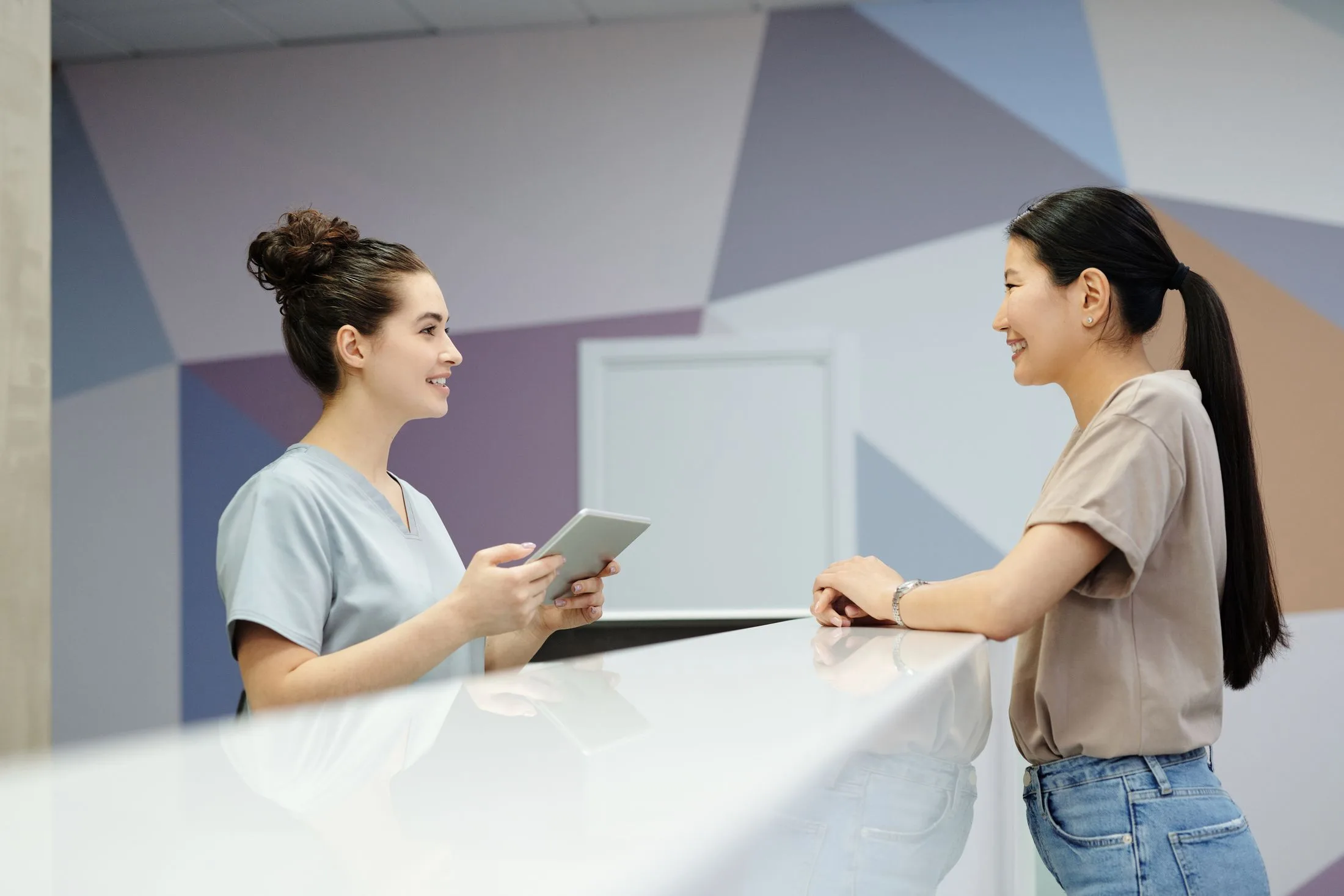 Nurse at a modern front desk greeting a patient, tablet in hand