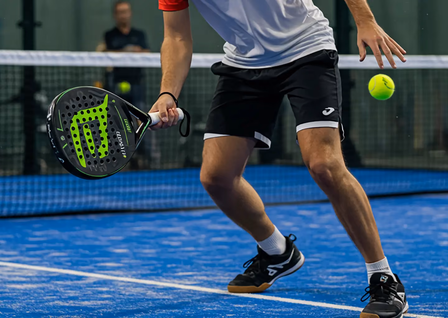 Close-up of a padel player in action, positioning to hit a ball during a competitive match on a blue indoor court.
