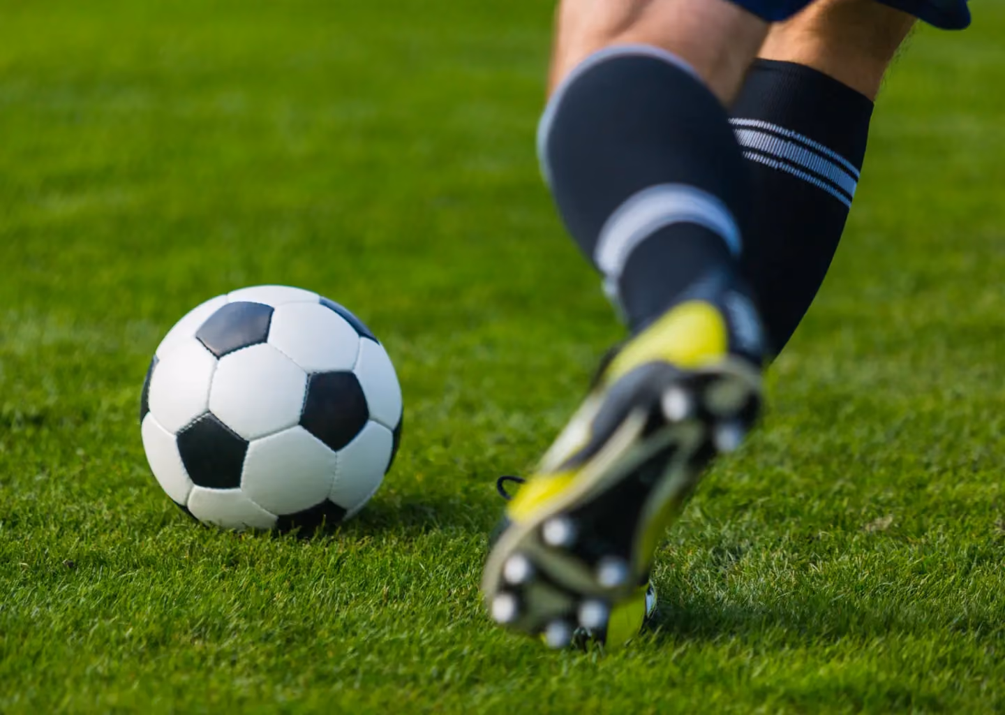 Close-up of a soccer player approaching a football on a grass field, moments before striking the ball during play.