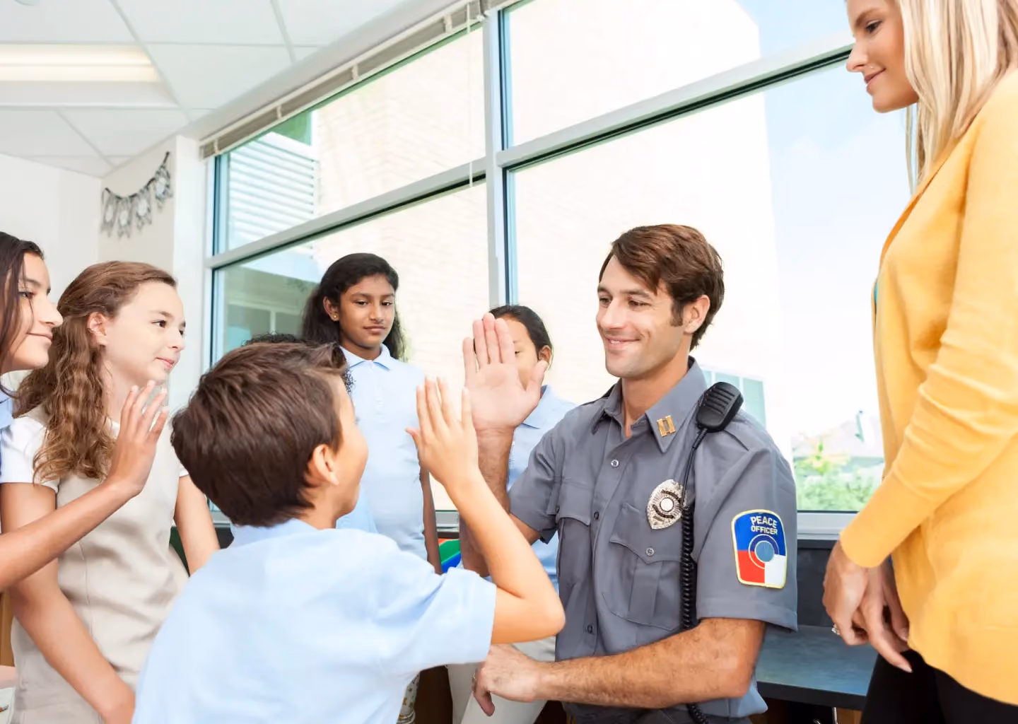 A school safety officer interacting with students in a classroom, giving a high-five to a child.