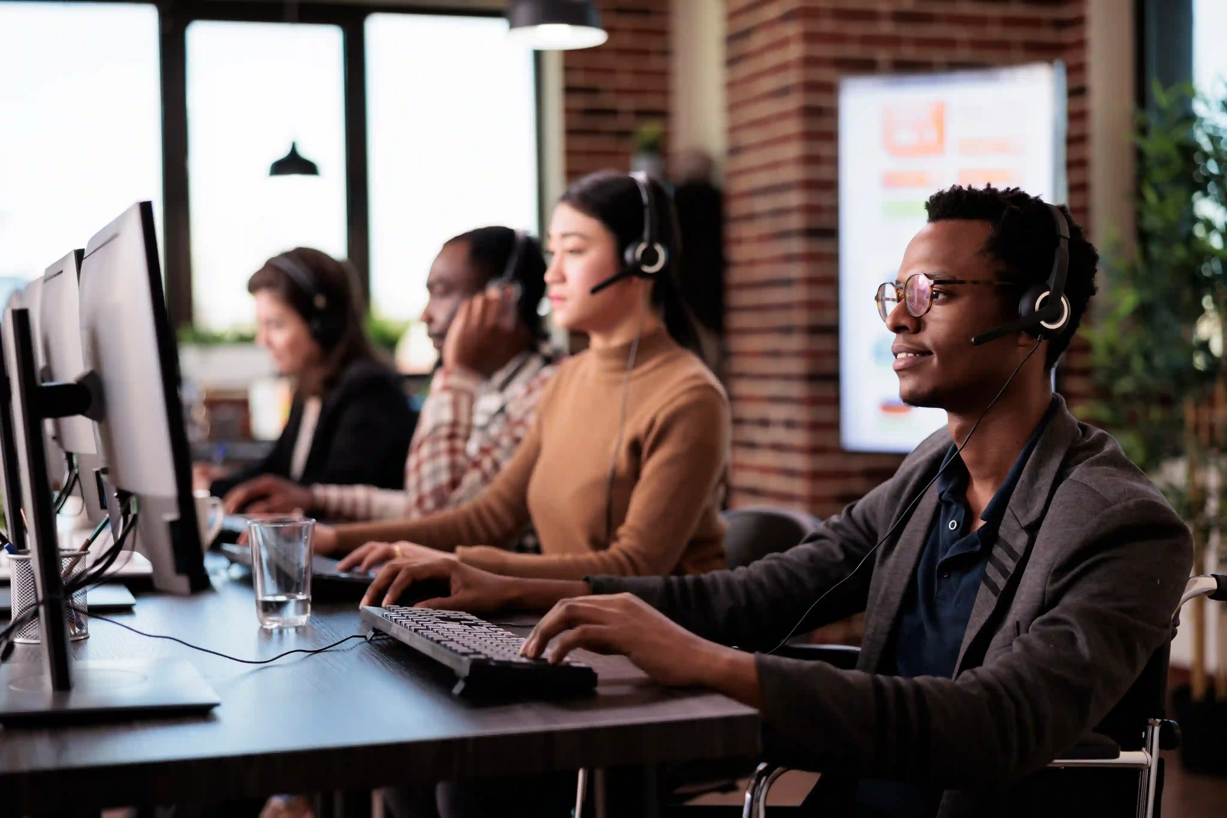 Customer support agents wearing headsets assisting customers from desktop computers in a modern contact center.