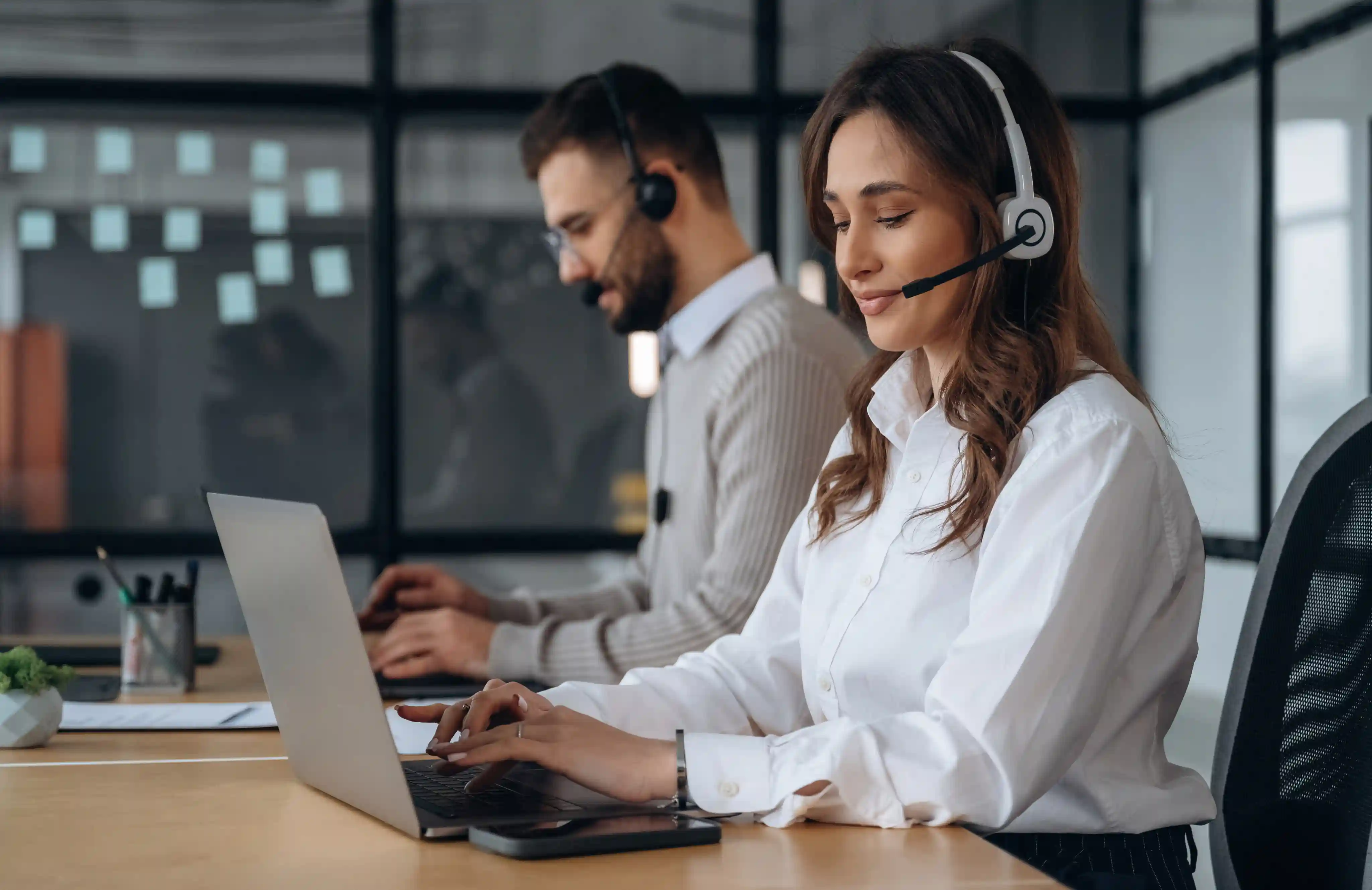 Customer service representatives wearing headsets providing support from laptops in a modern office.