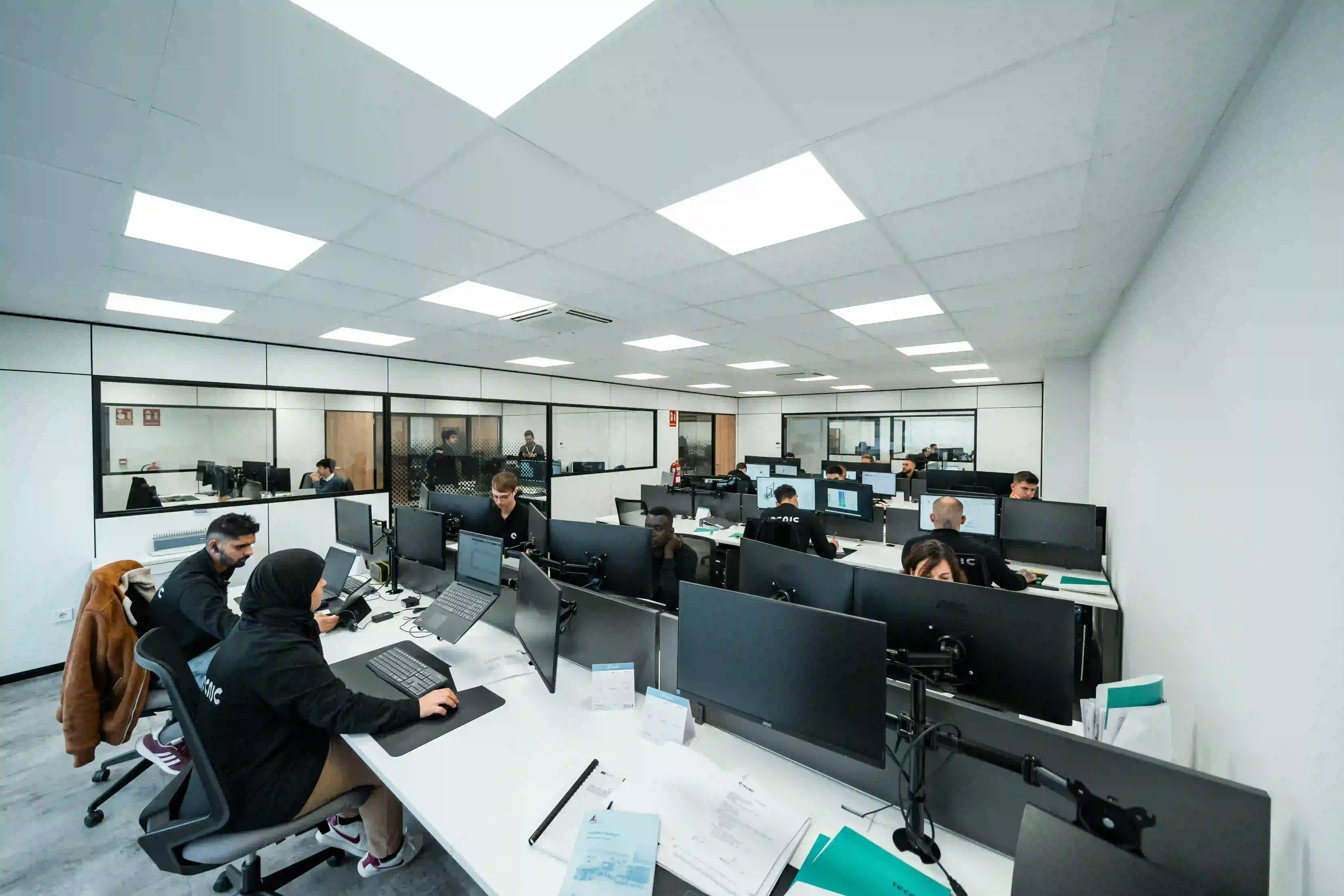 Open-plan office with employees working at computer workstations.