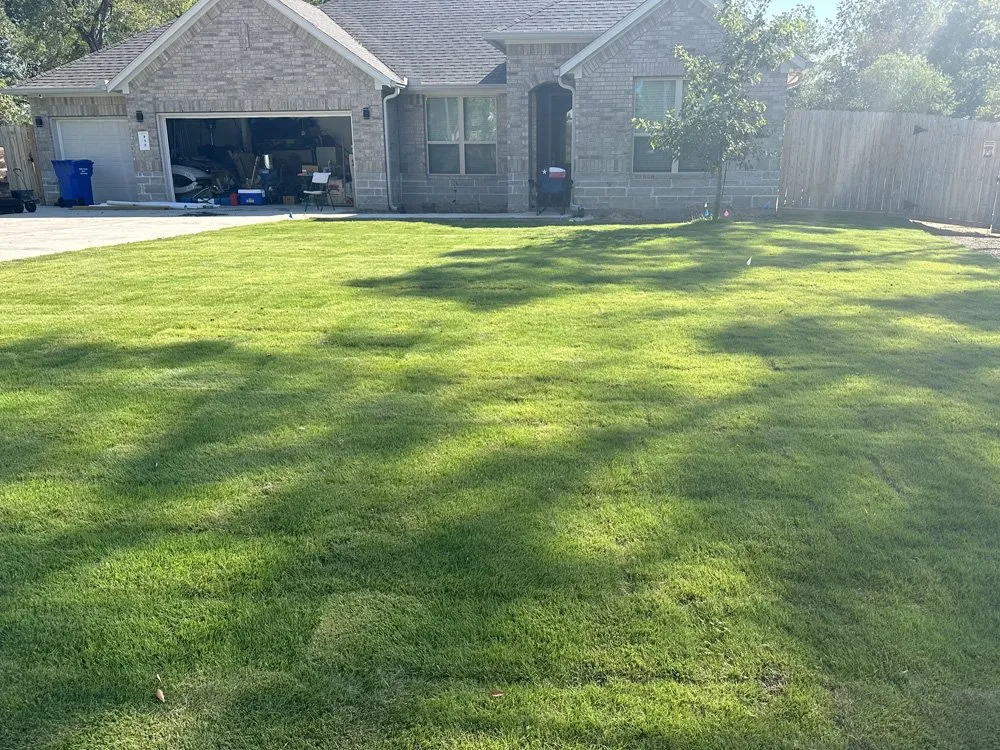Front yard with freshly installed green lawn in front of a brick house with an open garage.