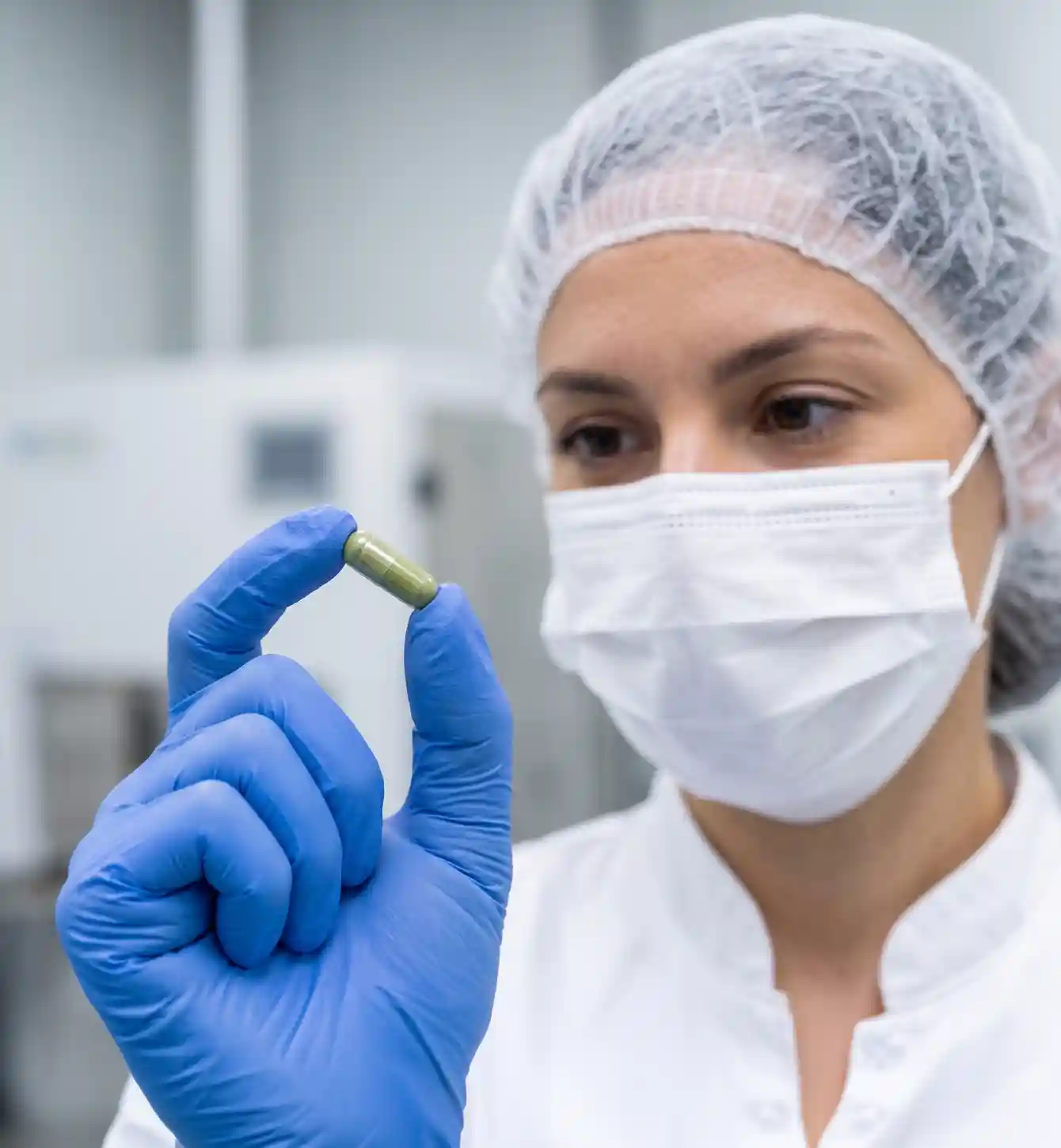 Technician in a hairnet and face mask inspecting a product sample