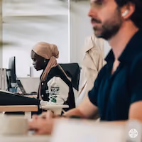 Deux personnes concentrées travaillant sur des ordinateurs dans un bureau moderne ouvert.