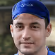 Portrait d'un homme portant un bandana bleu, souriant légèrement avec un fond flou.