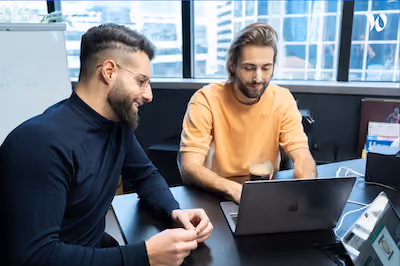 Nicolas et Thomas, fondateurs de Dishop discutent devant un ordinateur portable dans un bureau moderne avec grandes fenêtres.