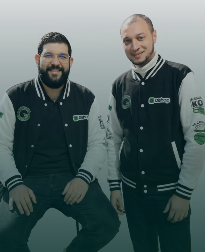 Deux hommes souriants portent des vestes noires et blanches avec des logos dont 'Dishop', posant devant un fond uni clair.