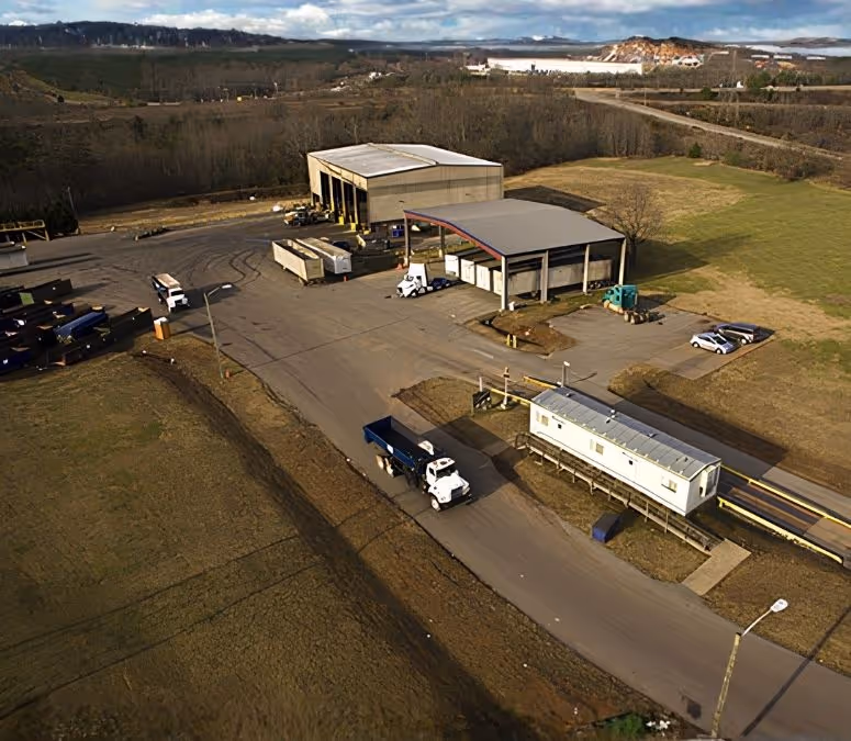 Aerial view of a waste transfer facility with trucks, service buildings, and surrounding grassy areas.