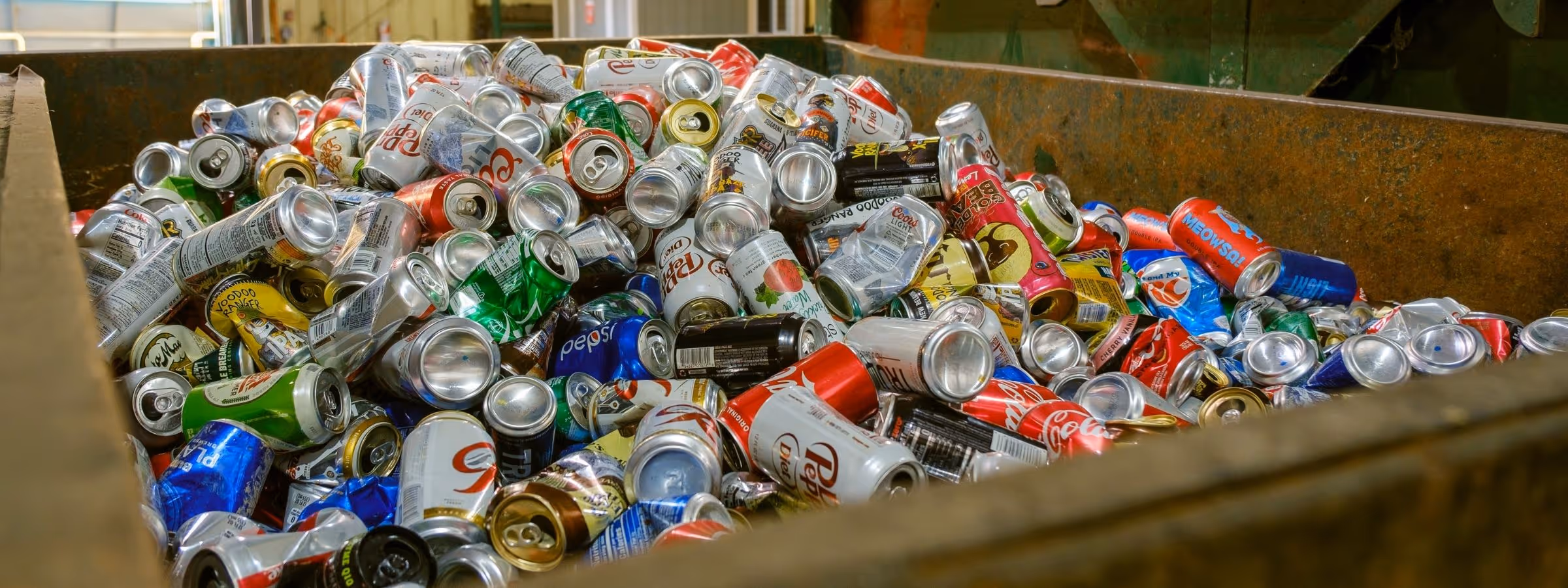 Large container filled with crushed and whole aluminum cans for recycling in a processing facility.
