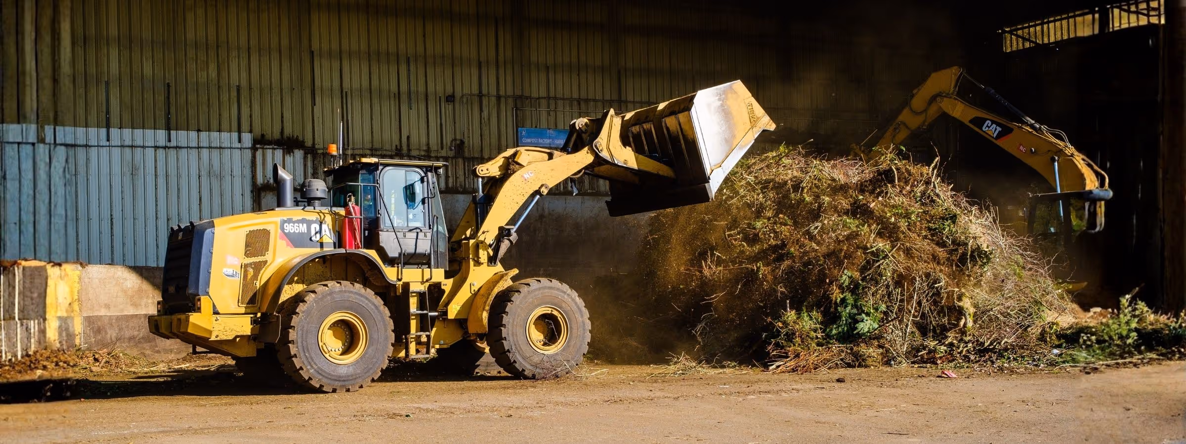 Yellow wheel loader moving a large pile of yard waste inside a storage facility.