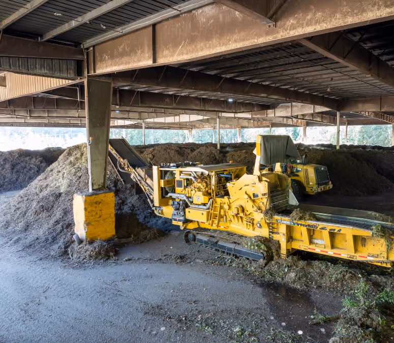 Yellow compost shredder machine inside a large covered facility with piles of organic waste.