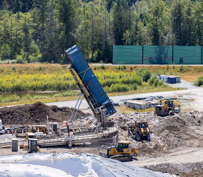 A blue truck unloading waste at a landfill site with bulldozers and piles of soil and trash.