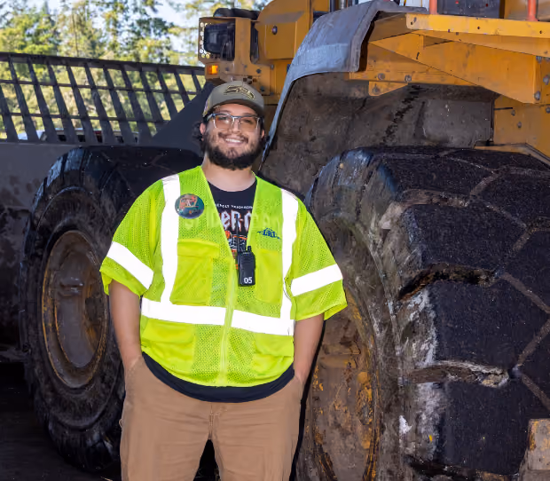 Man wearing a neon yellow safety vest and cap standing in front of large construction machinery tires.