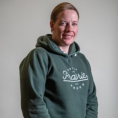 Woman smiling wearing a green hoodie with white text reading "Proud to be in the Prairies."