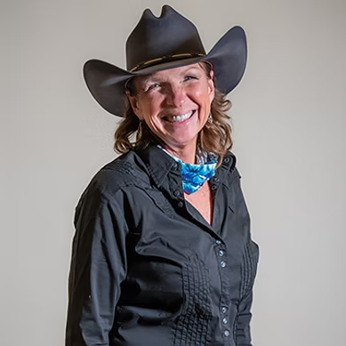 Smiling woman wearing a black cowboy hat, black shirt, and blue patterned neckerchief.