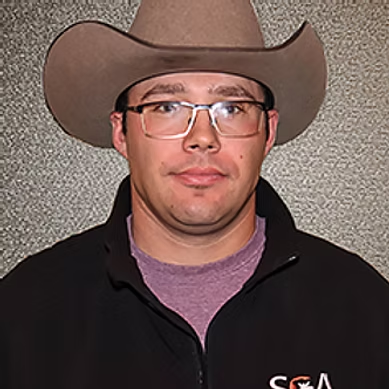 Man wearing glasses, a brown cowboy hat, and a black jacket with an SCA logo on a gray background.