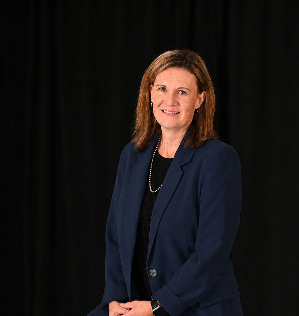Woman with shoulder-length hair wearing a navy blazer, black top, and pearl necklace, smiling at camera.
