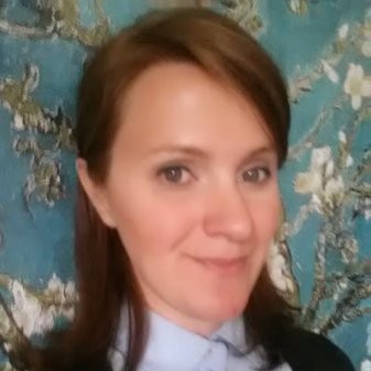Woman with light brown hair smiling slightly, wearing a collared shirt with a floral background.