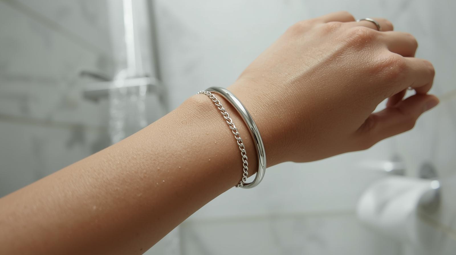 Close-up of wrist with silver bangle and chain bracelet exposed to water in shower.