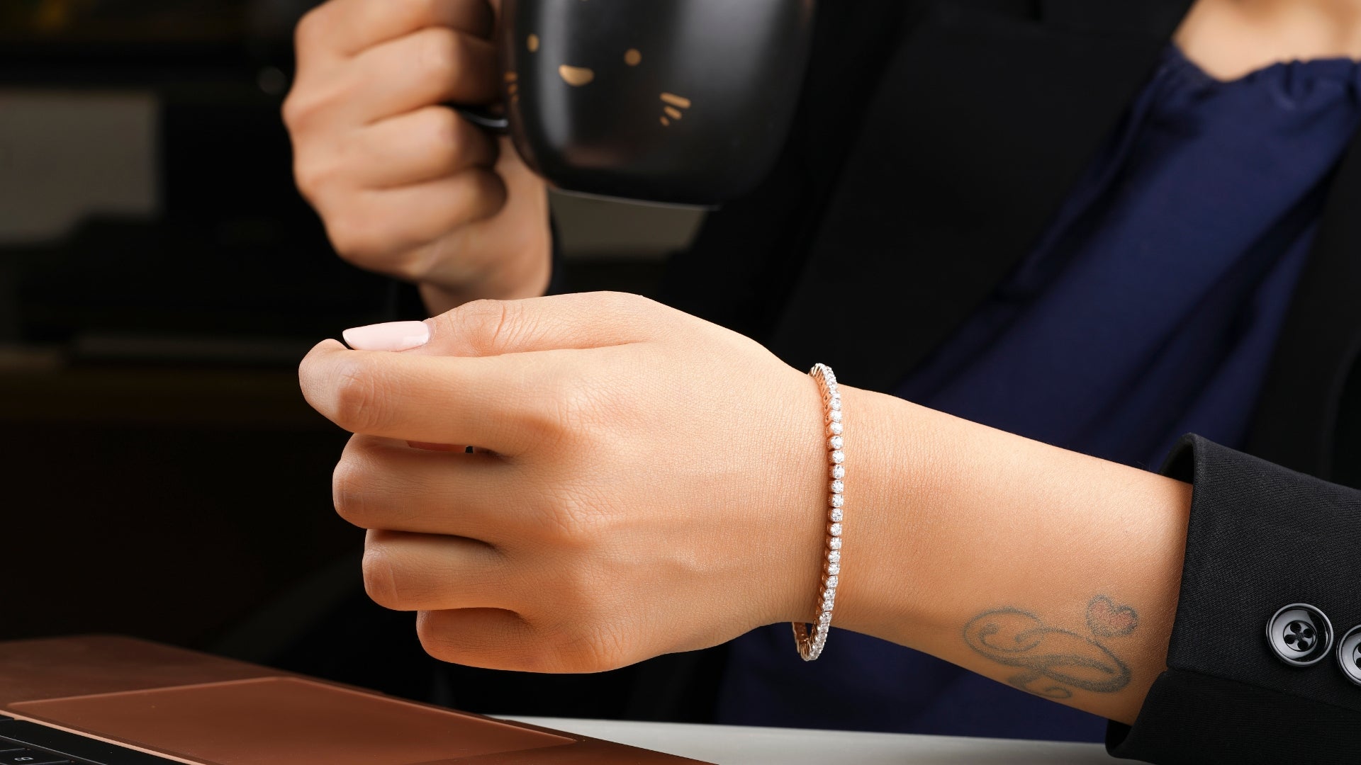 Elegant silver tennis bracelet with gemstones on a woman’s wrist while holding a coffee mug.