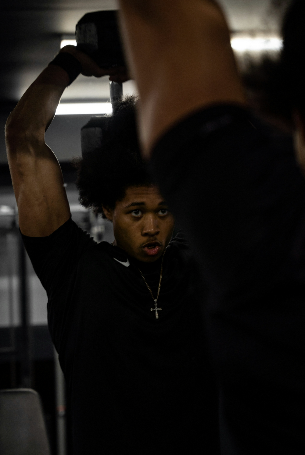 Man lifting a dumbbell overhead while wearing a silver cross necklace