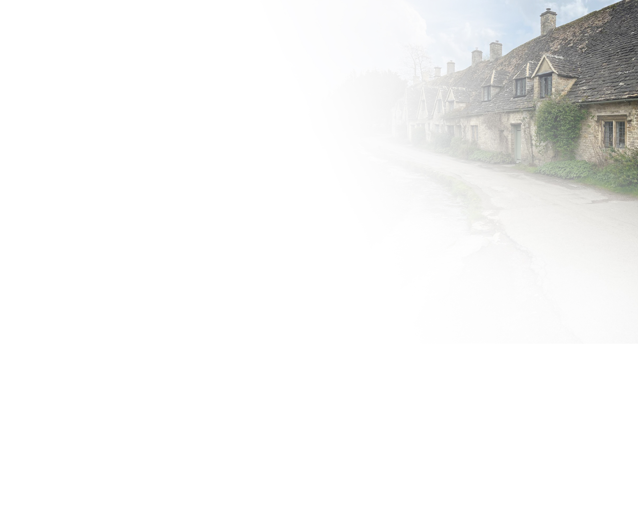 Row of old stone cottages with chimneys along a quiet road on a misty day.
