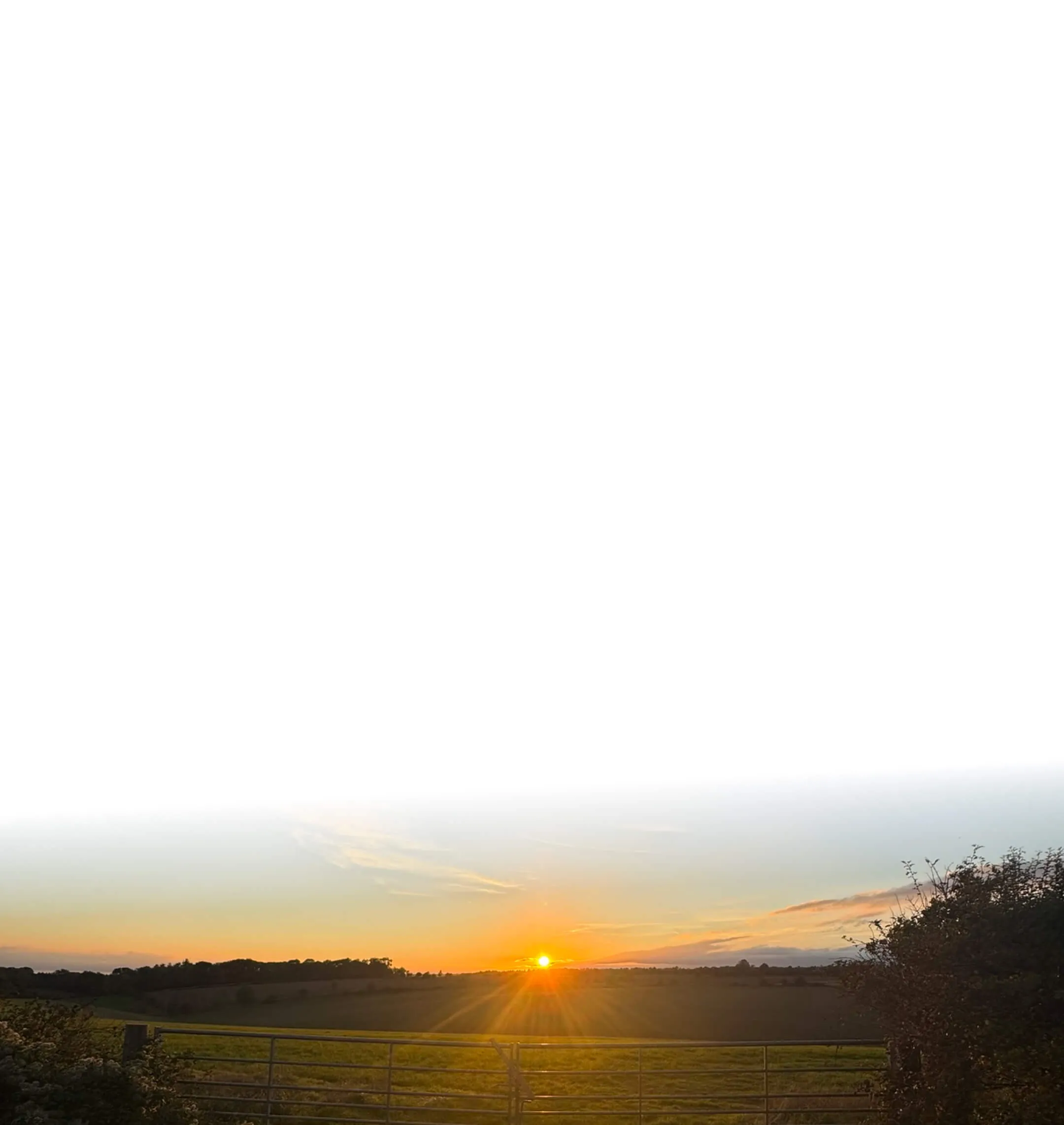 Sunset over Cotswold countryside field, orange glow beaming over a farm gate.