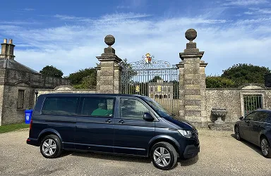 Tour vehicle, parked outside large gates at Lodge Park, blue sky.